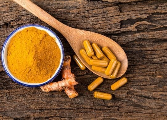 the turmeric powder , capsule and roots curcumin on wooden plate